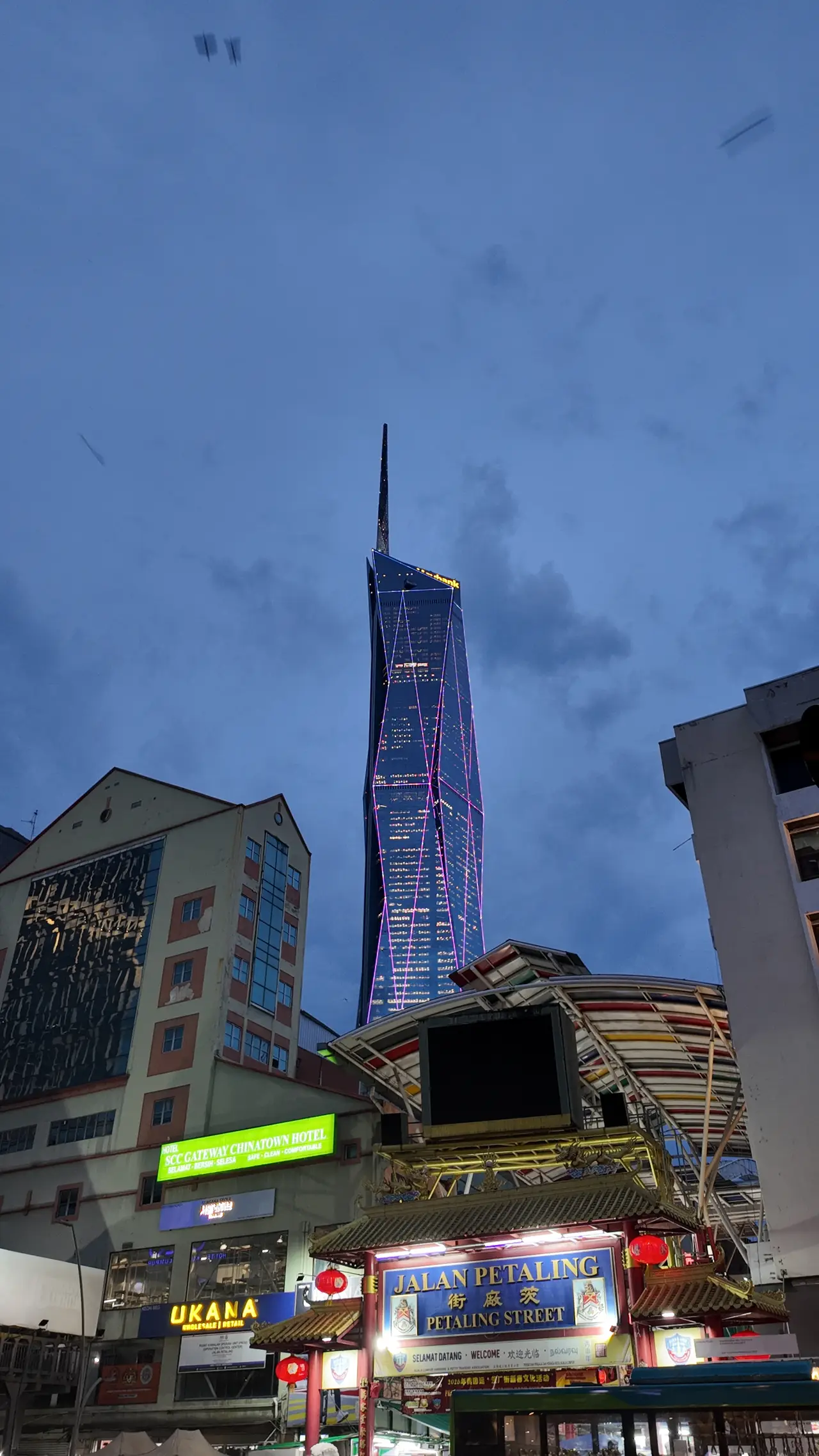 Merdeka 118 towering over the neon signs of Petaling Street at dusk